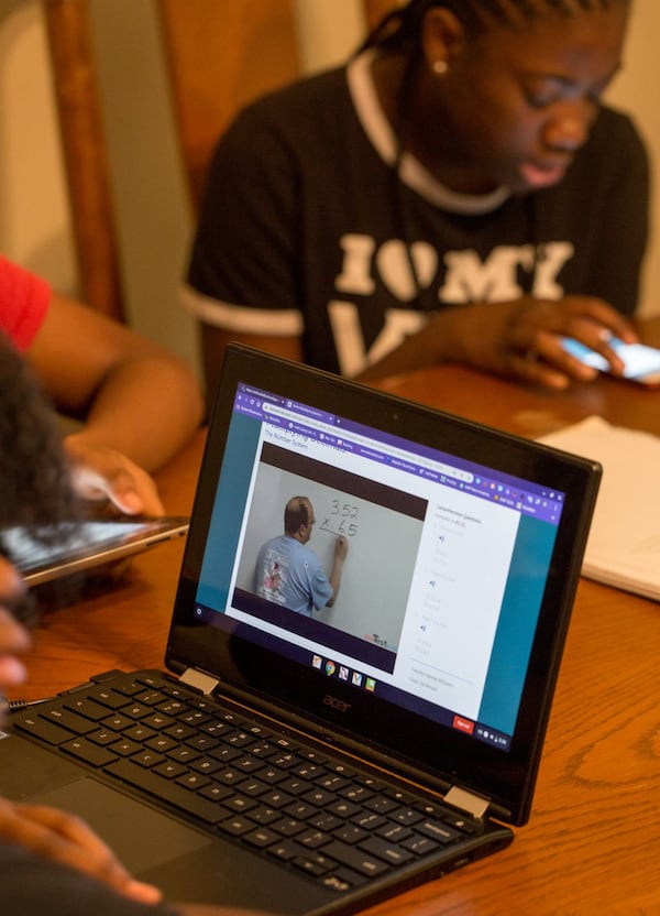 Raina Hill, 12, front computer, a 6th grader at Champion Middle School logs in and gets started on long division lessons while her sister Roniyah Hill, 15, a 10th grader at Martin Luther King High School uses her phone to look up definitions. (Jenni Girtman for Atlanta Journal Constitution)