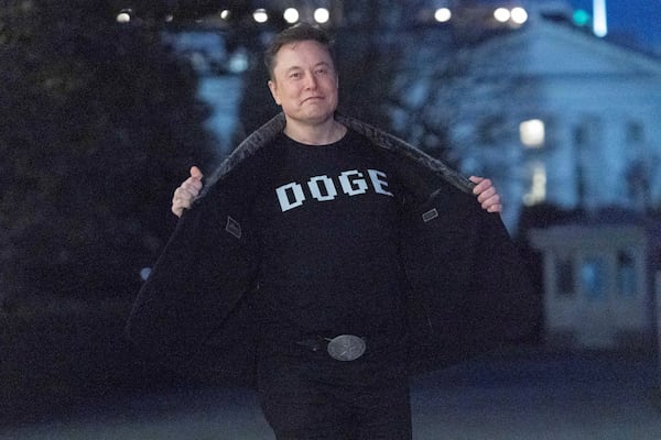 Elon Musk flashes his t-shirt that reads "DOGE" to the media as he walks on South Lawn of the White House, in Washington, Sunday, March 9, 2025. (AP Photo/Jose Luis Magana)