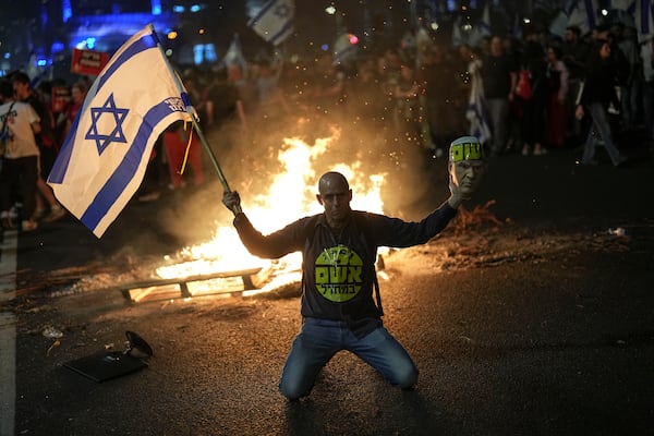 A protester holds an Israeli flag as Israelis light a bonfire during a protest after Prime Minister Benjamin Netanyahu has dismissed his defense minister Yoav Gallant in a surprise announcement in Tel Aviv, Israel, Tuesday, Nov. 5, 2024. (AP Photo/Francisco Seco)