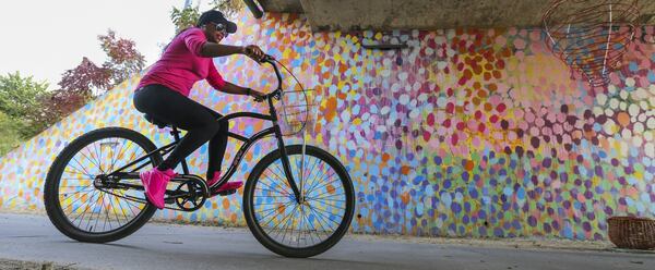 Monique Lee of College Park rides her bike along the Beltline near Piedmont Park. The mural behind her was painted by Alex Brewer. Also known as the artist Hense, he has several colorful murals in the Atlanta area. One of the most popular murals is this one under Virginia Avenue near Piedmont Park. JOHN SPINK /JSPINK@AJC.COM