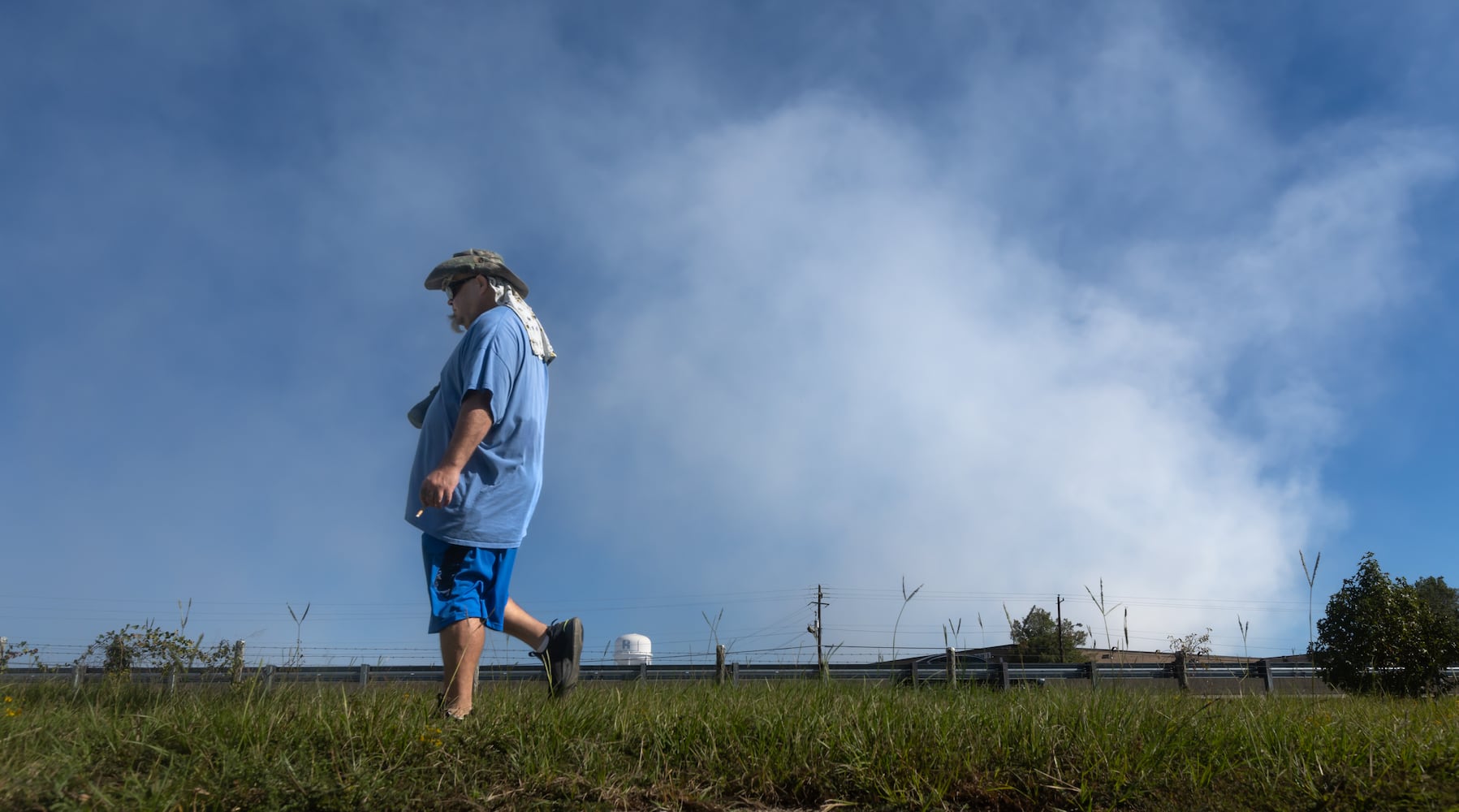 Darryl Shumake walks along Iris Drive at mid-morning Wednesday, Oct 2, 2024 as a large mile-long plume was still visible over Conyers as crews worked at the plant that caught on fire days earlier. But as the sun lifted above the horizon, so did the shelter-in-place order for Rockdale County residents. Those living nearby have been advised to stay inside every evening through early morning until Friday. (John Spink/AJC)