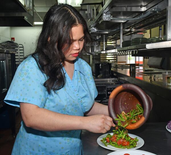 Ilene Rouamvongsor, a Lao American, is a recipe developer, food stylist and food educator. Here, she pours her Thum Mak Tua (Long Bean Salad) from a kok and sak (Lao for mortar and pestle). The kok and sak is a common item found in a typical Lao home and used to prepare dishes where ingredients need varying crushing and bruising to bring maximum flavor to the ingredients. (Chris Hunt for the AJC)