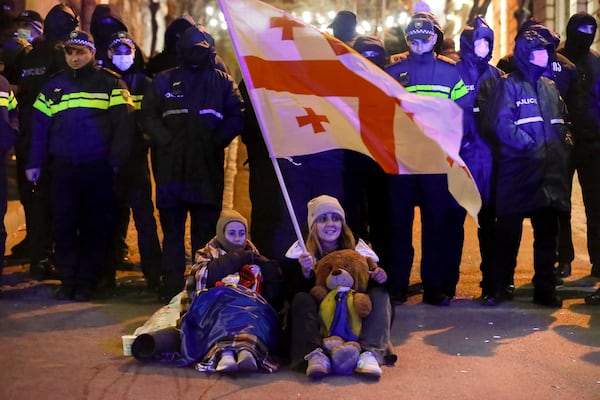 A woman and a girl sit holding a Georgian national flag in front of police blocking the entrance of the Parliament's building during a rally to demand new parliamentary elections in the country, in Tbilisi, Georgia, on Monday, Nov. 25, 2024. (AP Photo/Zurab Tsertsvadze)