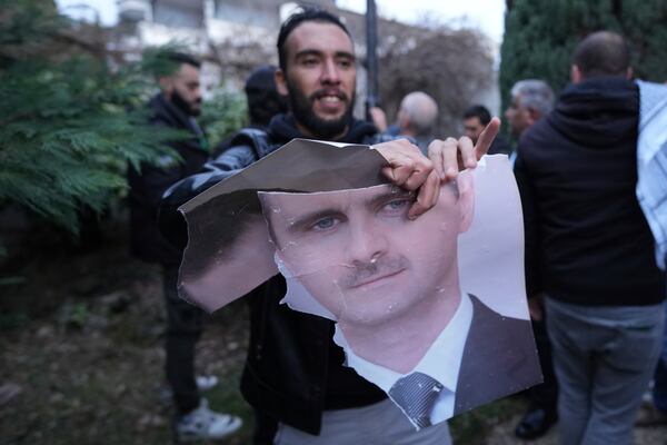 A man tears up a photo of Syrian President Bashar Assad in front of the Syrian embassy in Belgrade, Serbia, Sunday, Dec. 8, 2024. (AP Photo/Darko Vojinovic)