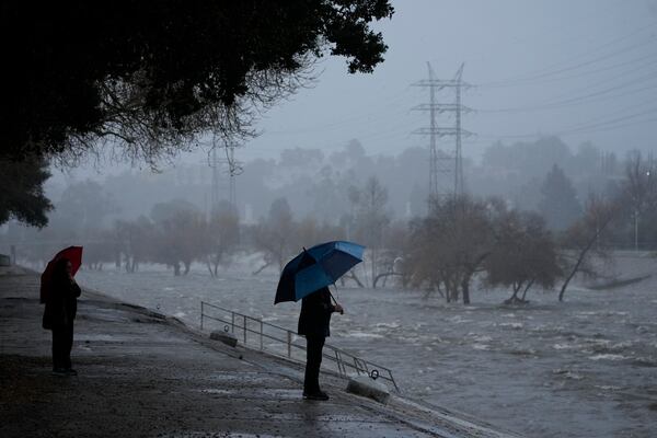 FILE - A couple walks on the edge of the Los Angeles River on Feb. 4, 2024, as an atmospheric rivers batters Los Angeles. (AP Photo/Damian Dovarganes, File)