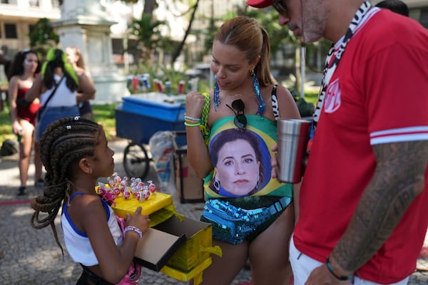 A reveler dons a Brazilian national flag designed with an image of actress Fernanda Torres at a pre-Carnival street party paying tribute to the Oscar-nominated actress for her role in "I'm Still Here", in Rio de Janeiro, Sunday, Feb. 23, 2025. (AP Photo/Silvia Izquierdo)