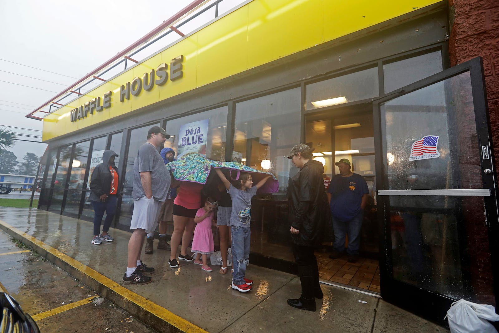 FILE - Luke Churchill, left, stands with his wife, Mary and their children, Katie, 13, Liam, 9, and Raighan, 3, as they wait in the rain outside an open Waffle House restaurant in Wilmington, N.C., after Hurricane Florence traveled through the area, Sept. 16, 2018. (AP Photo/Chuck Burton, File)