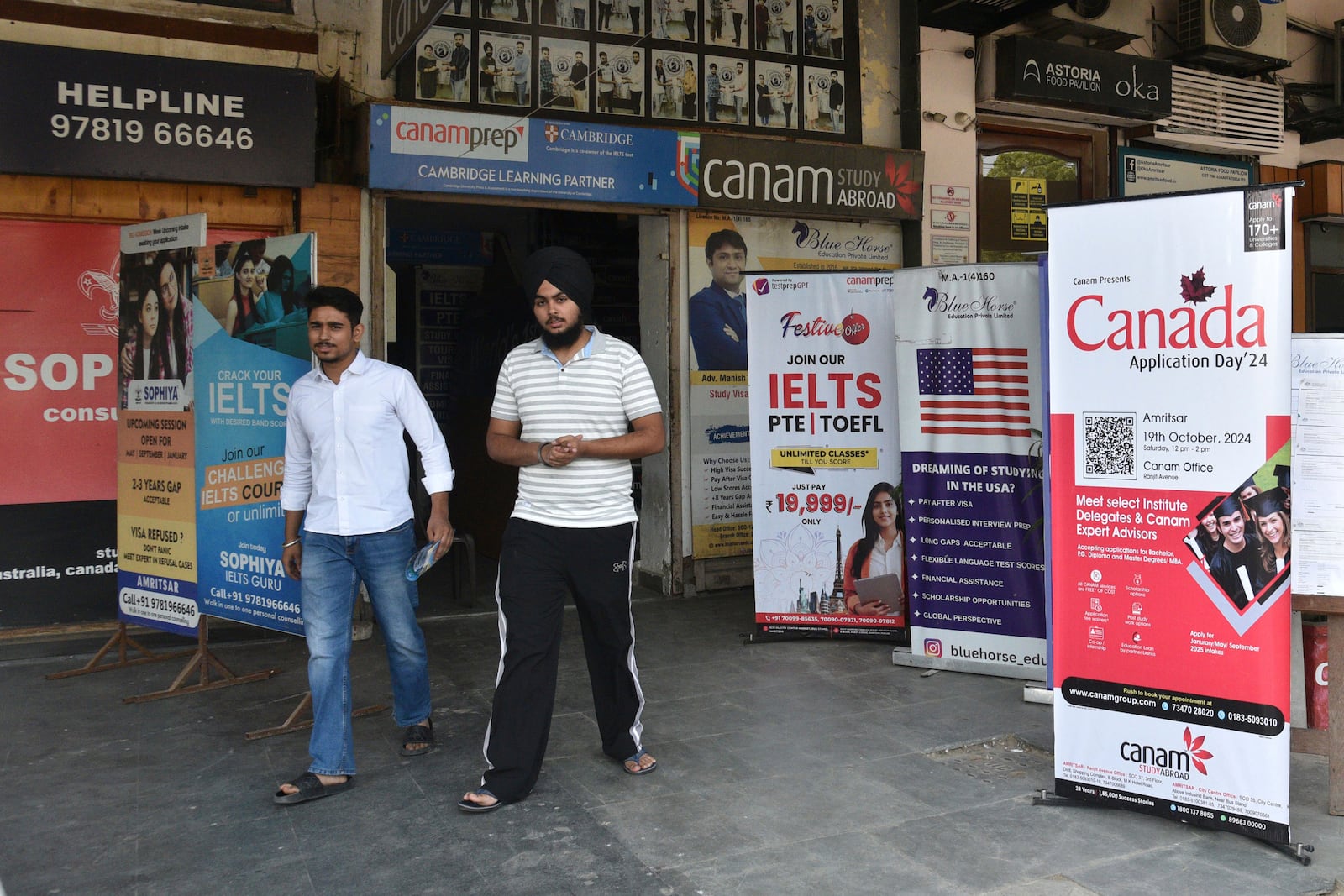 People walk past banners inviting students to study in Canada and other places abroad at a market in Amritsar, in the northern Indian state of Punjab, Tuesday, Oct. 15, 2024. (AP Photo/Prabhjot Gill)