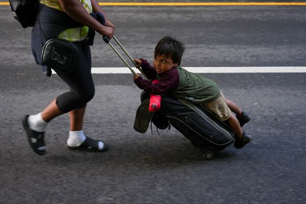 A child holds on to luggage as migrants walk along the highway in Huixtla, southern Mexico, heading toward the country's northern border and ultimately the United States, Thursday, Nov. 7, 2024. (AP Photo/Moises Castillo)