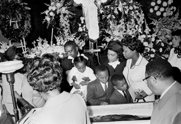 An unidentified man lifts Bernice King, 5, over her father's casket in Atlanta, April 7, 1968. Her father, Dr. Martin Luther King, Jr., was slain by sniper fire in Memphis, Tenn., April 4. Bernice's brothers, Martin III and Dexter, and her mother, Coretta Scott King, center, wearing hat, also view the body.