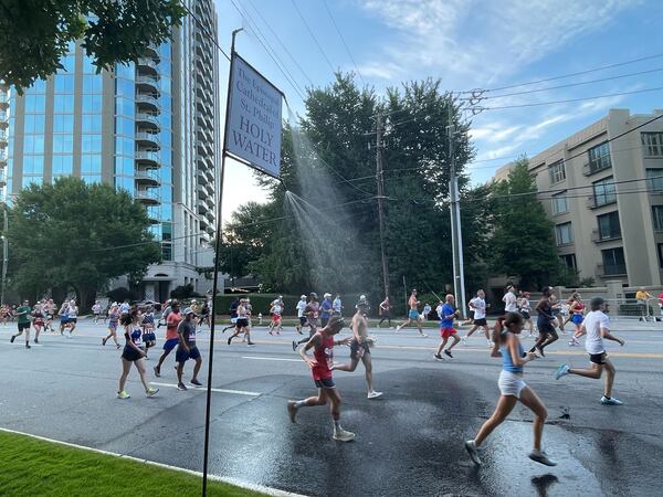 As racers passed the Cathedral of St. Philip, they were offered blessings of holy water, either sprinkled by the Rev. Sam Candler, dean of the Cathedral, or from a holy water mister set up above Peachtree Street.  “Blessings, blessings, blessings!” Candler said to runners as they passed. (Anisah Muhammad / AJC)