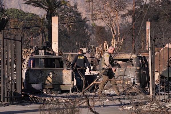 A medical examiner and sheriff's deputies check on a home destroyed by the Eaton Fire on Saturday, Jan. 11, 2025, in Altadena, Los Angeles. (AP Photo/Mark J. Terrill)