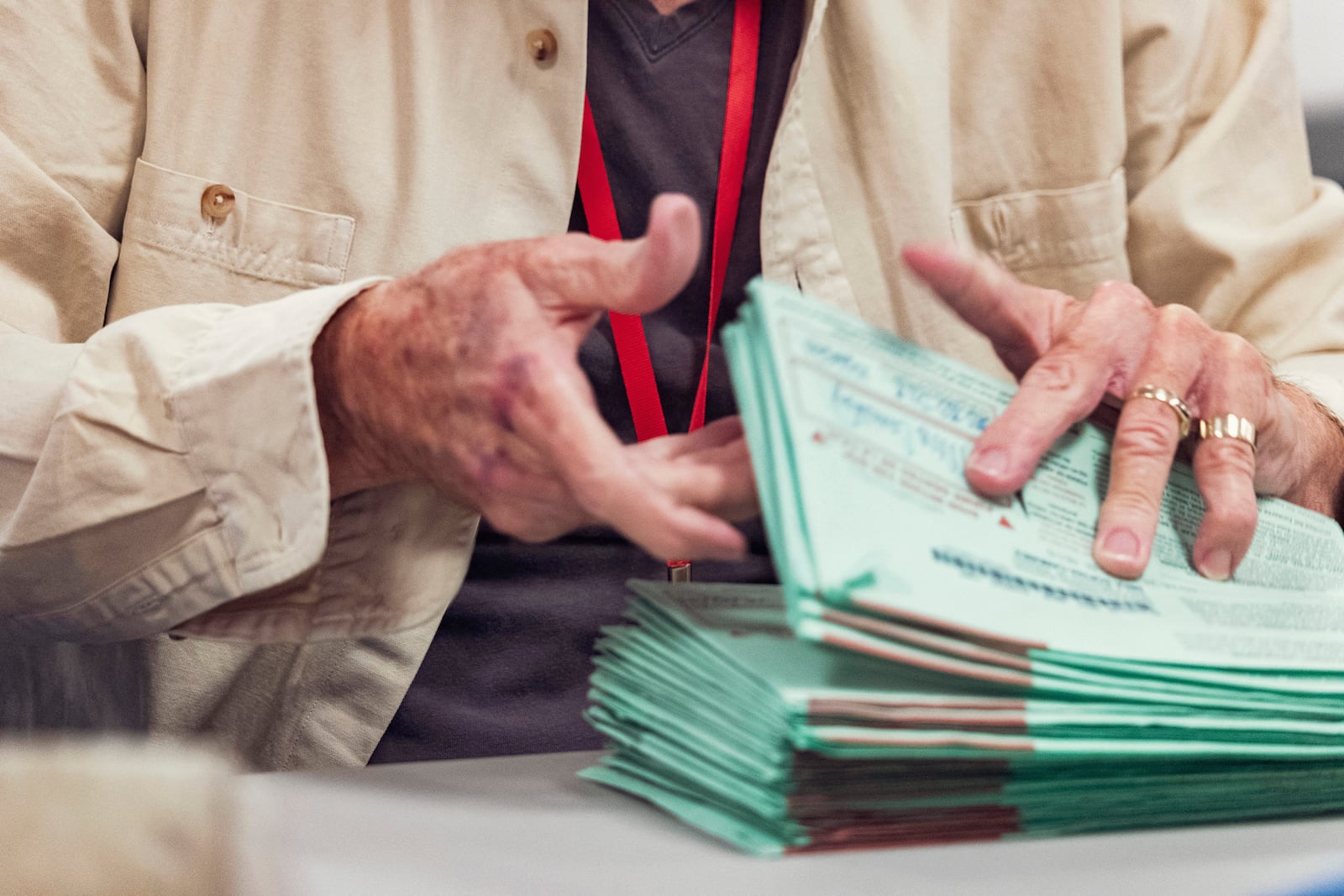 An election worker wearing a red lanyard holds a stack of 2024 General Election ballots in their envelopes to be opened and sorted at the Maricopa County Tabulation and Election Center in Phoenix on Oct. 23, 2024. Election workers wear colored lanyards to designate their party: red for registered Republicans, yellow for Independents and blue for Democrats. (Olivier Touron/AFP/Getty Images/TNS)