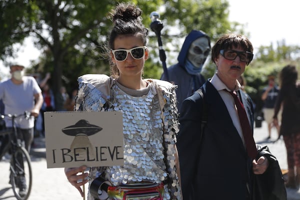 A woman (2nd L) holds a banner with an UFO painted on it and reading "I believe" as another protester dressed up as alien (3rd R) walks by at a demonstration against conspiracy theorists at Mauerpark, amidst the novel coronavirus COVID-19 pandemic, in Berlin, on May 30, 2020. (Odd Andersen/AFP/Getty Images/TNS)