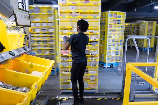 An employee pulls an item from a pod of merchandise at Amazon’s robotic fulfillment center in Stone Mountain on Wednesday, Oct. 23, 2024. Amazon’s roots in robotics stretch back to 2012. (Ben Gray for the AJC)