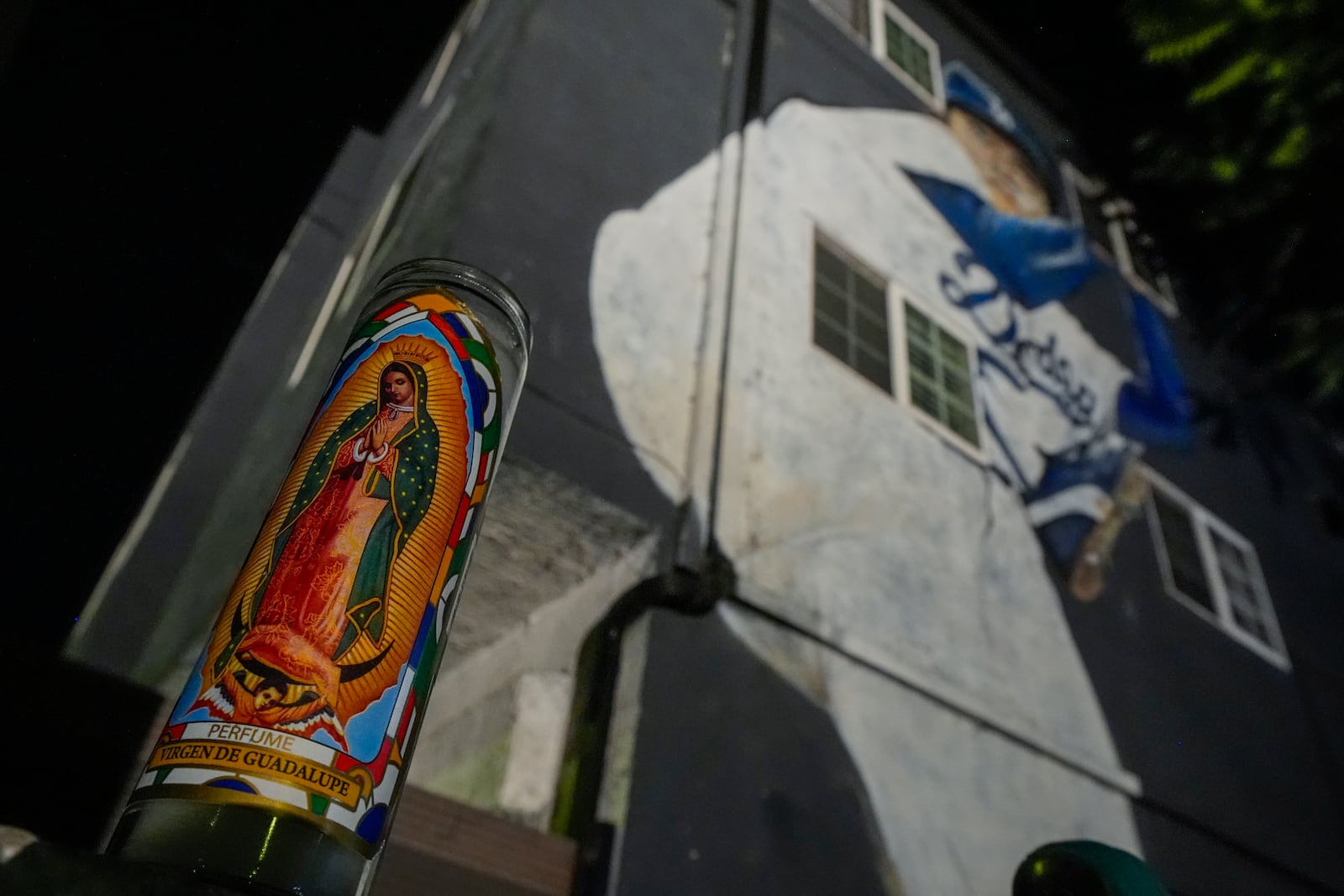 A votive candle donning an image of the Virgen de Guadalupe sits near a mural depicting former Los Angeles Dodgers pitcher Fernando Valenzuela, Tuesday, Oct. 22, 2024, in Los Angeles. (AP Photo/Julio Cortez)