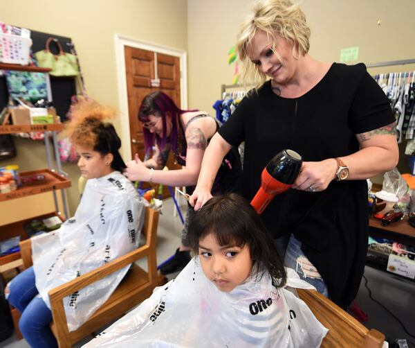 Stylist Trish Moree works on Belinda Dominguez, 3, as her sister Liliana Ginorio, 12, get her hair styled by Kara Chapman on Monday. Liliana is going into the seventh grade, as Belinda will be starting at Buford Head Start. Matthew Miller, of Matthew’s & Co. Salon in Flowery Branch, brought 22 local stylists and assistants to give more than 100 free haircuts on Monday to get kids ready for school. It was a partnership with North Gwinnett Co-op, which helps families in need. KENT D. JOHNSON / KDJOHNSON@AJC.COM