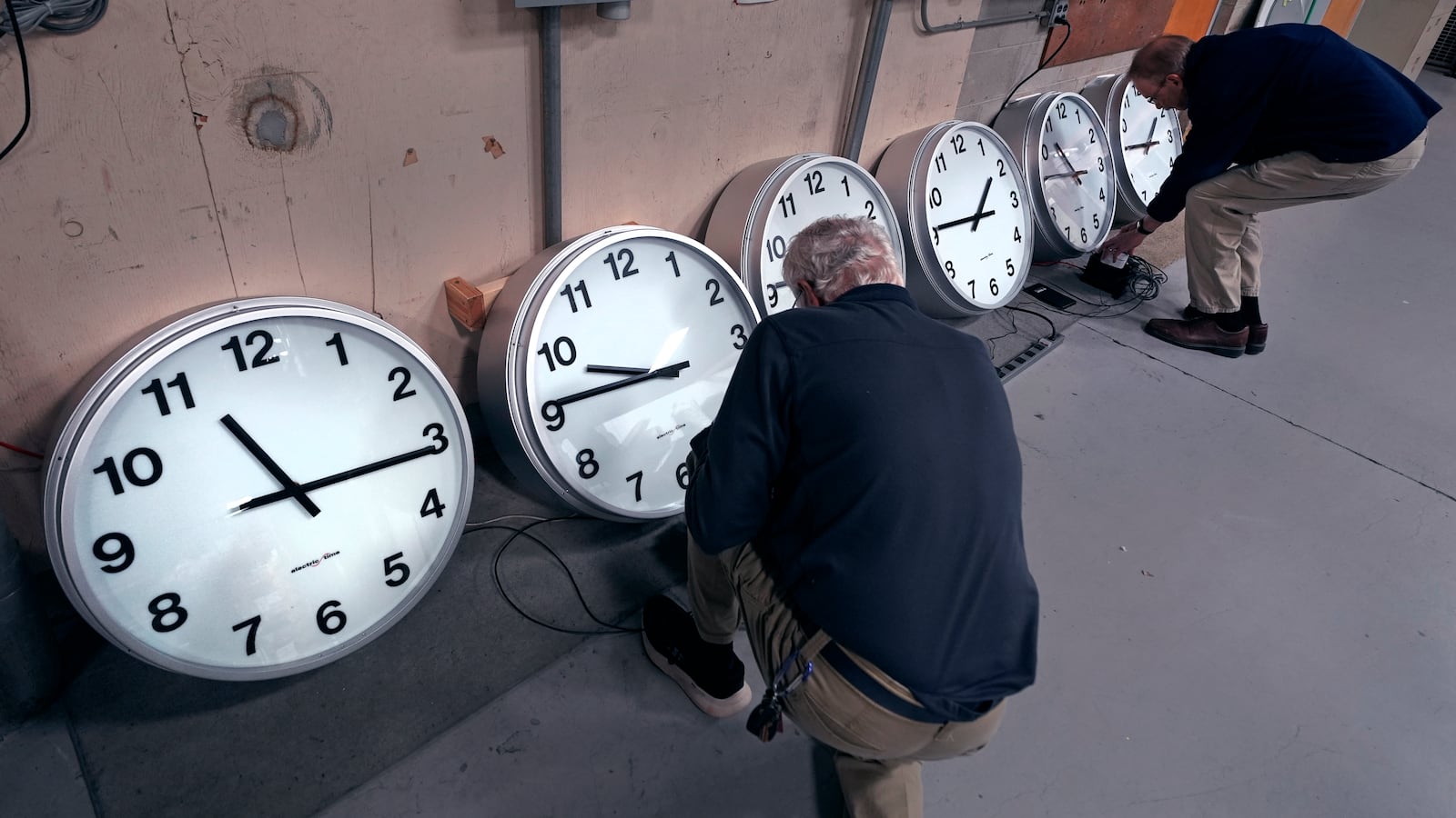 Clockmakers Rich Finn, left, and Tom Erb adjust the time zone controllers on a series of clocks that'll be installed at Paine Field in Everett, Wash., at the Electric Time Company, Wednesday, Oct. 30, 2024, in Medfield, Mass. (AP Photo/Charles Krupa)