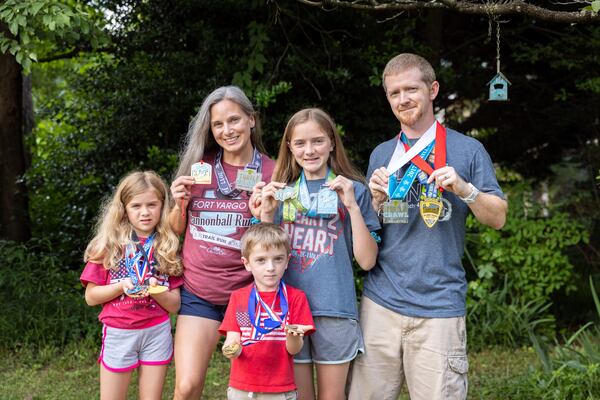 (L-R) Libby, 9; mother Ashley; James, 5; Abby, 12, and dad John Coleman pose with medals from races at their home in Decatur on Thursday, May 23, 2024.  (Arvin Temkar / AJC)