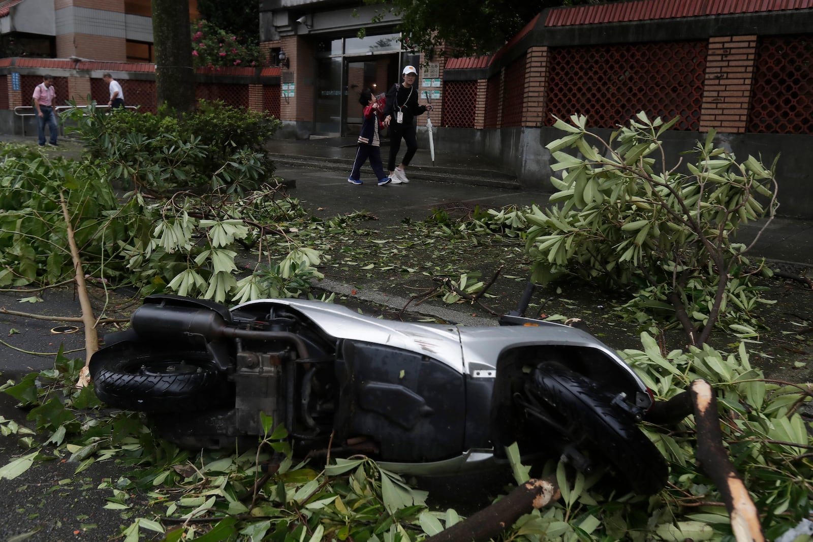 A mother and a son walk past an upside down motorbike after Typhoon Kong-rey leaves in Taipei, Taiwan, Friday, Nov. 1, 2024. (AP Photo/Chiang Ying-ying)