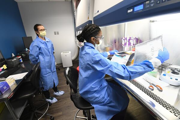 Leah Roberts opens up a delivery of COVID-19 samples for testing from a local practice as fellow Molecular Biologist Aubrey Kellison looks on, at Ipsum Diagnostics labratory on Monday, March 23, 2020. Kellison is training in order to take procedures back to West Virginia to implement. JOHN AMIS / FOR THE AJC