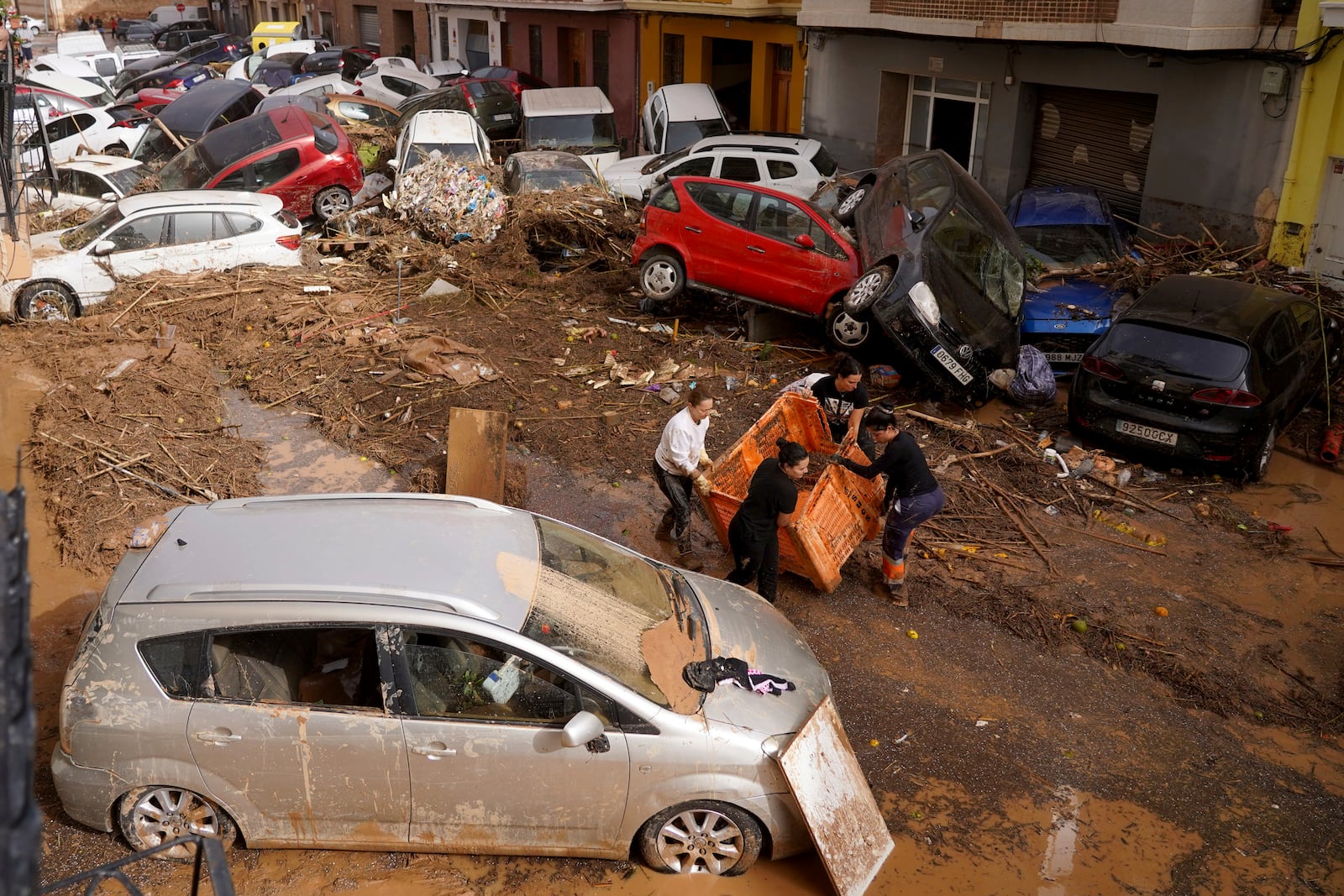 Residents clean the street next to cars piled up after being swept away by floods in Valencia, Spain, Wednesday, Oct. 30, 2024. (AP Photo/Alberto Saiz)