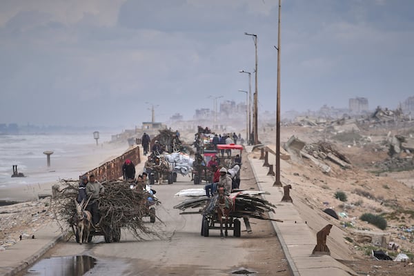 Displaced Palestinians, carrying their belongings, wood and other items, move between southern and northern Gaza along a beach road away from the areas where the Israeli army is operating after Israel's renewed offensive in the Gaza Strip, in the outskirts of Gaza City, Friday March 21, 2025. (AP Photo/Abdel Kareem Hana)