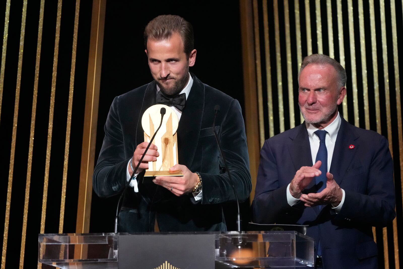 England's player Harry Kane, left, is flanked by former German player Karl-Heinz Rummenigge as he receives the Gerd Mueller trophy during the 68th Ballon d'Or (Golden Ball) award ceremony at Theatre du Chatelet in Paris, Monday, Oct. 28, 2024. (AP Photo/Michel Euler)