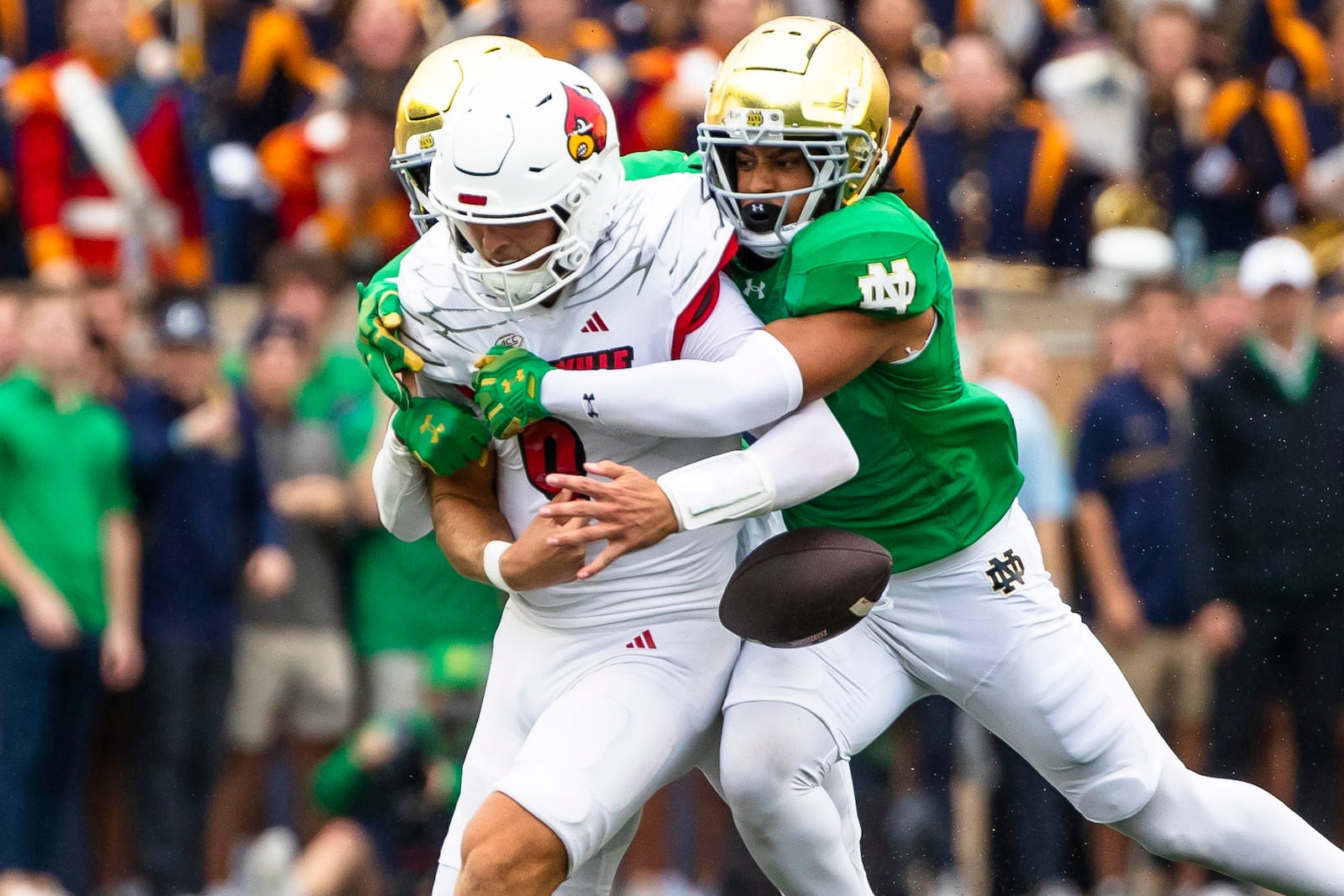 Notre Dame defensive back Leonard Moore, back, punches the ball away from Louisville quarterback Tyler Shough (9) as Notre Dame safety Xavier Watts, right, also tackles him during the first half of an NCAA college football game, Saturday, Sept. 28, 2024, in South Bend, Ind. (AP Photo/Michael Caterina)