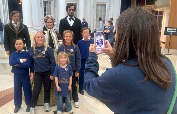 Michelle Bulow of Mokena, Ill., takes a photo of, from left, her daughters Allison Bulow, 10, Ellie Bulow, 5, and their friend Julia Kowolski, 10, in front of models of Abraham Lincoln and his family at the Abraham Lincoln Presidential Library and Museum on Thursday, Oct. 24, 2024, in Springfield, Ill. The girls are homeschooled and Michelle Bulow said they were visiting the museum as part of their study of government and democratic elections. (AP Photo/John O'Connor)