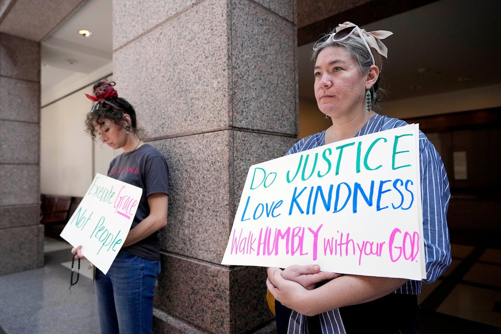 Sascha Anderson, right, and Sam McRae, left, hold signs as they stand outside a room where a committee is discusing the case of death row inmate Robert Roberson, Monday, Oct. 21, 2024, in Austin, Texas. (AP Photo/Tony Gutierrez)