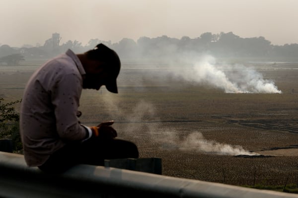 A person checks his mobile phone as farmers burn crop residue after harvest near Bundelkhand expressway some 330 kilometers (206 miles) from New Delhi, India, Sunday, Nov. 17, 2024. (AP Photo/Manish Swarup)