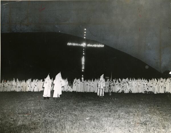 B/W copy of a photo taken in 1948: Hooded Ku Klux Klansmen gather around a huge flaming cross as the Klan held one of its largest initiation ceremonies in its life. In the background looms Stone Mountain. (ACME TELEPHOTO/AJC FILES)