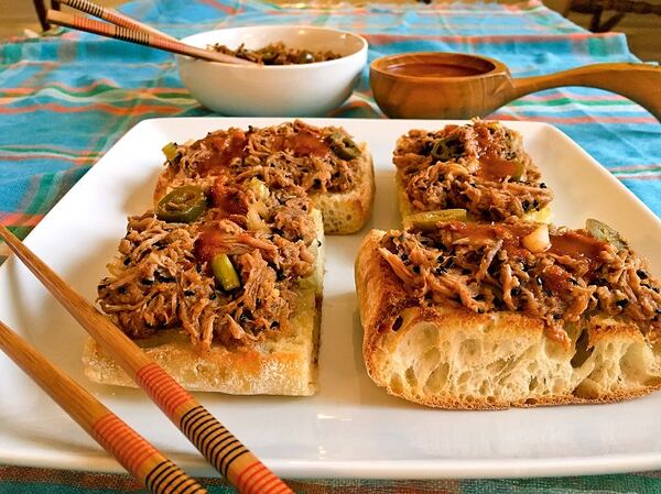 Korean-style Pulled Pork Pizza with a ladle of extra spicy sauce and a bowl of extra pork flanking the square plate of four pieces of pizza. (Karen Kane/ Pittsburgh Post-Gazette/TNS)