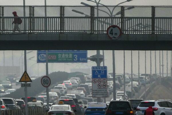 A resident walks across a pedestrian overhead bridge as motorists clogged with heavy traffic on a city highway shrouded with pollution haze in Beijing, Saturday, March 1, 2025. (AP Photo/Andy Wong)