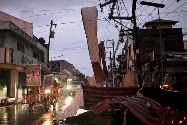 Motorists ride past a part of a roof suspended on electric wires blown by strong winds caused by Typhoon Man-yi along a street in the municipality of Baler, Aurora province, Philippines, Monday, Nov. 18, 2024. (AP Photo/Noel Celis)