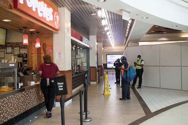 04/14/2020 - Atlanta, Georgia  - Individuals order food inside the domestic terminal food court at Hartsfield-Jackson International Airport in Atlanta, Tuesday, April 14, 2020. The temporary wall behind them (right) is covering the dining area which the airport closed recently to encourage social distancing. (ALYSSA POINTER / ALYSSA.POINTER@AJC.COM)