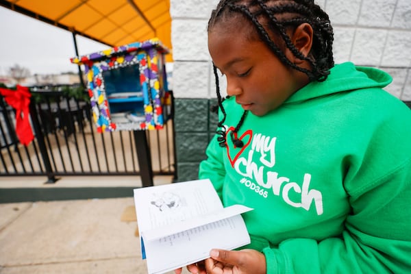 Kalynn Mills flips through the book that she got from the Little Free Libraries' Read in Color program outside the Eggs Up Grill in Morrow on Sunday, Dec. 17, 2023. (Miguel Martinez / miguel.martinezjimenez@ajc.com)