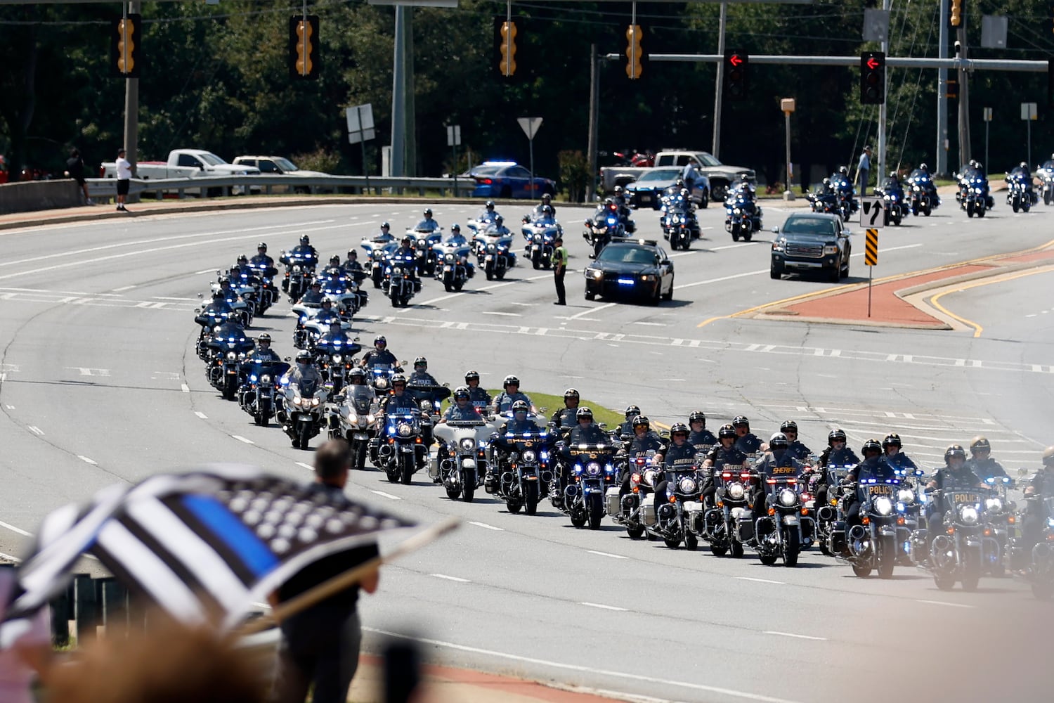 A  motorcade leads the procession of fallen Deputy Jonathan Koleski as people pay their respect with American flags over Chastain Rd on Wednesday, September 14, 2022. Miguel Martinez / miguel.martinezjimenez@ajc.com