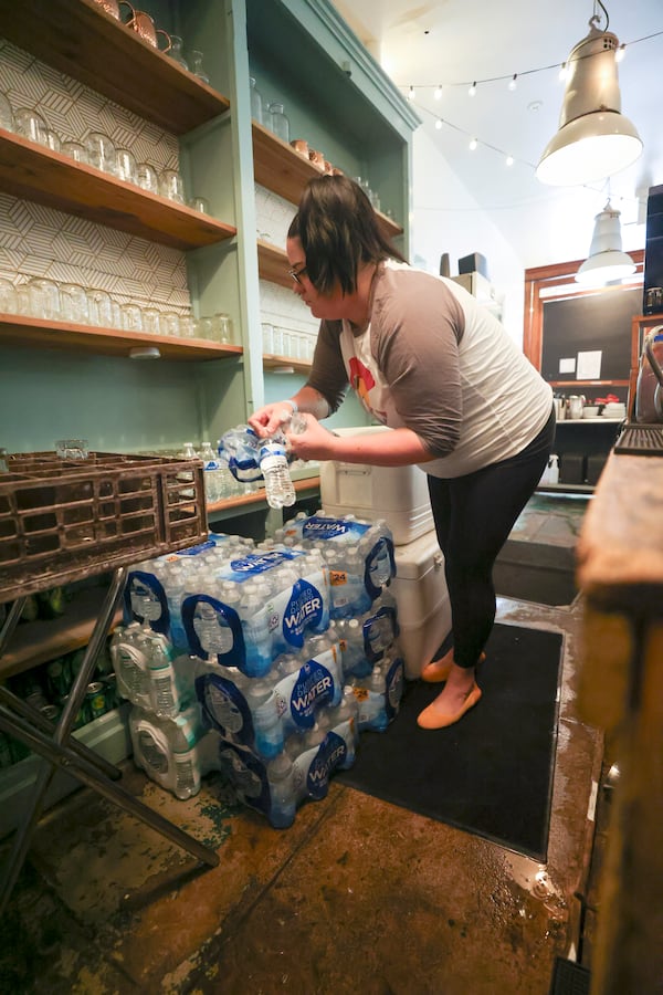 Sun in my Belly general manager Megan Cook takes bottled water out of the plastic bags for customers to use at the restaurant in the Kirkwood neighborhood, Monday, June 3, 2024, in Atlanta. The restaurant is still boiling large pots of water in the kitchen and using bottled waters for service. (Jason Getz / AJC)
