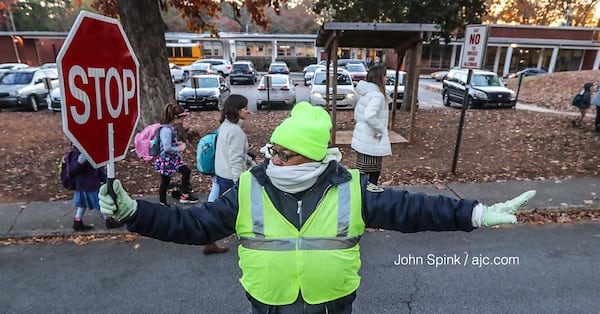 A crossing guard is bundled up to direct traffic outside Laurel Ridge Elementary School in DeKalb County, where some classrooms did not have heat Thursday. JOHN SPINK / JSPINK@AJC.COM