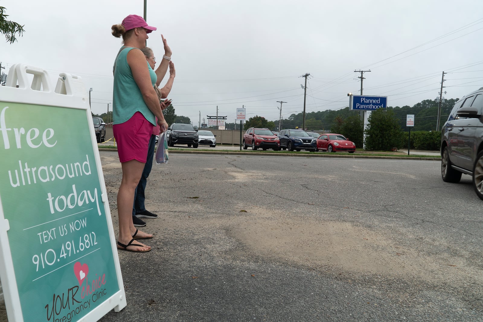 Air Force veteran and mother of two Laura Browne waves to a passing vehicle outside a Planned Parenthood clinic in Fayetteville, N.C., on Tuesday, Oct. 1, 2024. Browne does sidewalk ministry for a pregnancy center just up the road. (AP Photo/Allen G. Breed)