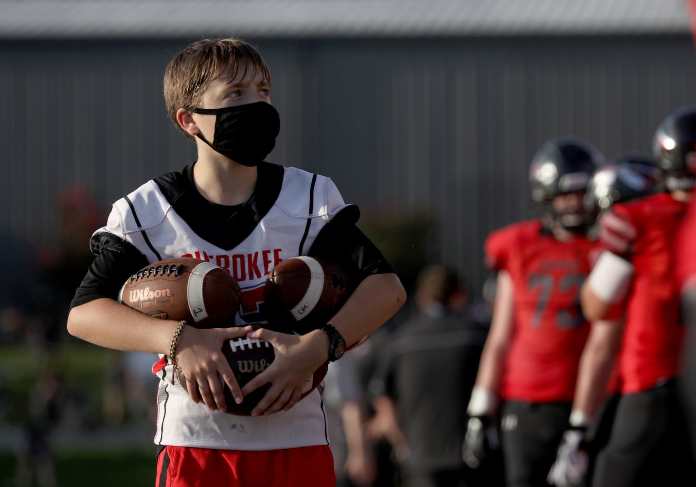 A Cherokee ball boy wears a mask as he carries footballs on the sideline in the first half of Cherokee's football game against Carver-Atlanta at Cherokee high school Wednesday, September 2, 2020 in Canton, Ga.. JASON GETZ FOR THE ATLANTA JOURNAL-CONSTITUTION