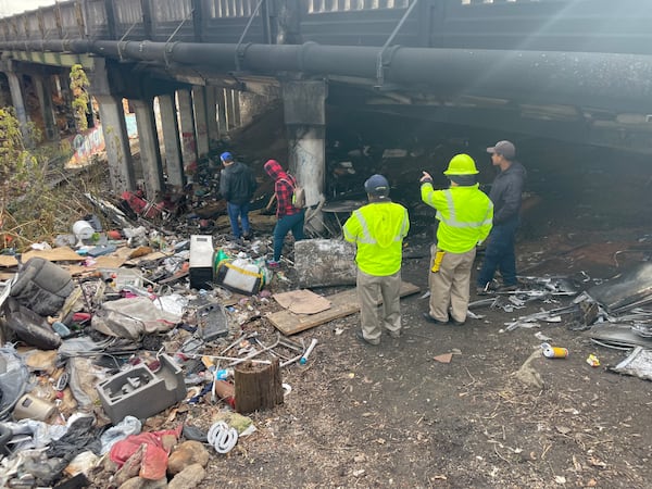 City employees and a cleanup crew inspect the remains of a homeless encampment built under a bridge on Cheshire Bridge. The encampment caught on fire last week, causing the closure of the road.