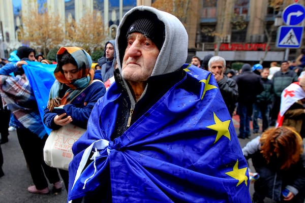 A protester with a EU flag on his shoulders stands in a street during a rally to demand new parliamentary elections in the country, near the Parliament's building in Tbilisi, Georgia, on Monday, Nov. 25, 2024. (AP Photo/Shakh Aivazov)