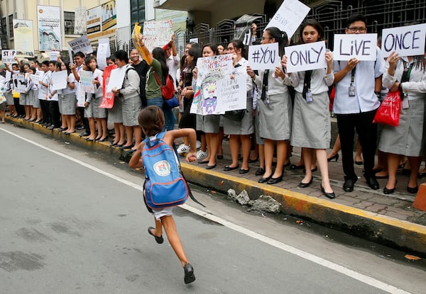 FILE- A school girl runs in front of students from St. Paul's University, a Roman Catholic school, as they come out from their campus to protest the killings being perpetrated in the unrelenting "War on Drugs" campaign of President Rodrigo Duterte, Friday, Sept. 30, 2016 in Manila, Philippines. (AP Photo/Bullit Marquez, File)