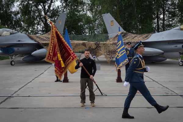 FILE - Ukraine's President Volodymyr Zelenskyy hands over the flag of a military unit on the occasion of the Air Forces Day against the background of Ukraine's Air Force's F-16 fighter jets in an undisclosed location in Ukraine, on Aug. 4, 2024. (AP Photo/Efrem Lukatsky, File)