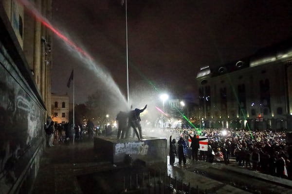 Demonstrators stand atop of a tomb under running water from a water cannon rallying outside the parliament's building to continue protests against the government's decision to suspend negotiations on joining the European Union in Tbilisi, Georgia, on Monday, Dec. 2, 2024. (AP Photo/Zurab Tsertsvadze)