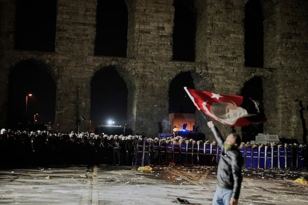 A man holds a Turkish flag with the image of Turkey's founding father Mustafa Kemal Ataturk in front of anti riot police officers during a protest against the arrest of Istanbul's Mayor Ekrem Imamoglu in Istanbul, Turkey, Friday, March 21, 2025. (AP Photo/Emrah Gurel)