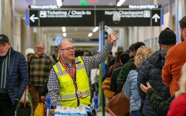 An airport worker hands out water to travelers waiting in long lines at Hartsfield-Jackson International Airport. Wednesday, January 22, 2025 (Ben Hendren for the Atlanta Journal-Constitution)